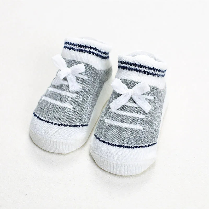 Pair of gray baby socks designed like sneakers with white bows and navy stripe details, featuring soft fabric and anti-slip soles for infants.